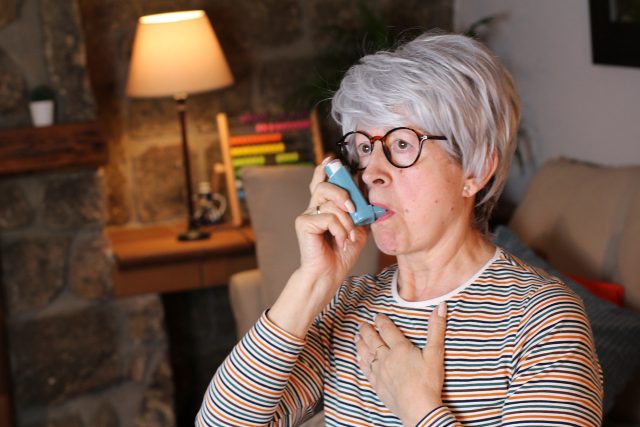 Senior woman using asthma inhaler at home